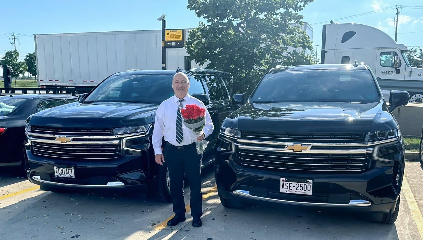 Lucian F. Muresanu, owner-operator of Contact Limo LLC, holding a bouquet of roses for an arriving client between two black late model luxury SUV SUVs