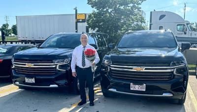 Lucian F. Muresanu, owner-operator of Contact Limo LLC, holding a bouquet of roses for an arriving client between two black late model luxury SUV SUVs