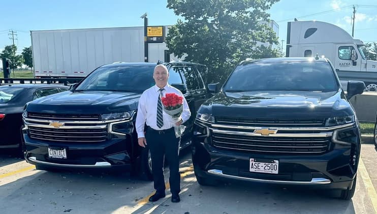 Lucian F. Muresanu, owner-operator of Contact Limo LLC, holding a bouquet of roses for an arriving client between two black late model luxury SUV SUVs